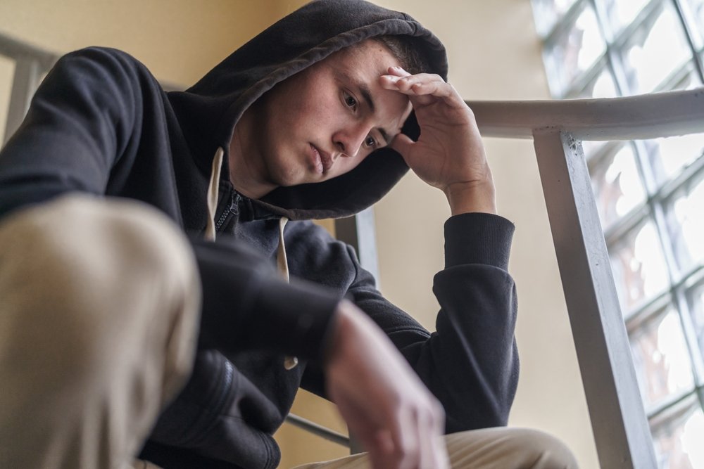 Young man sitting with his head resting on his hand, looking down, appearing tired or contemplative.